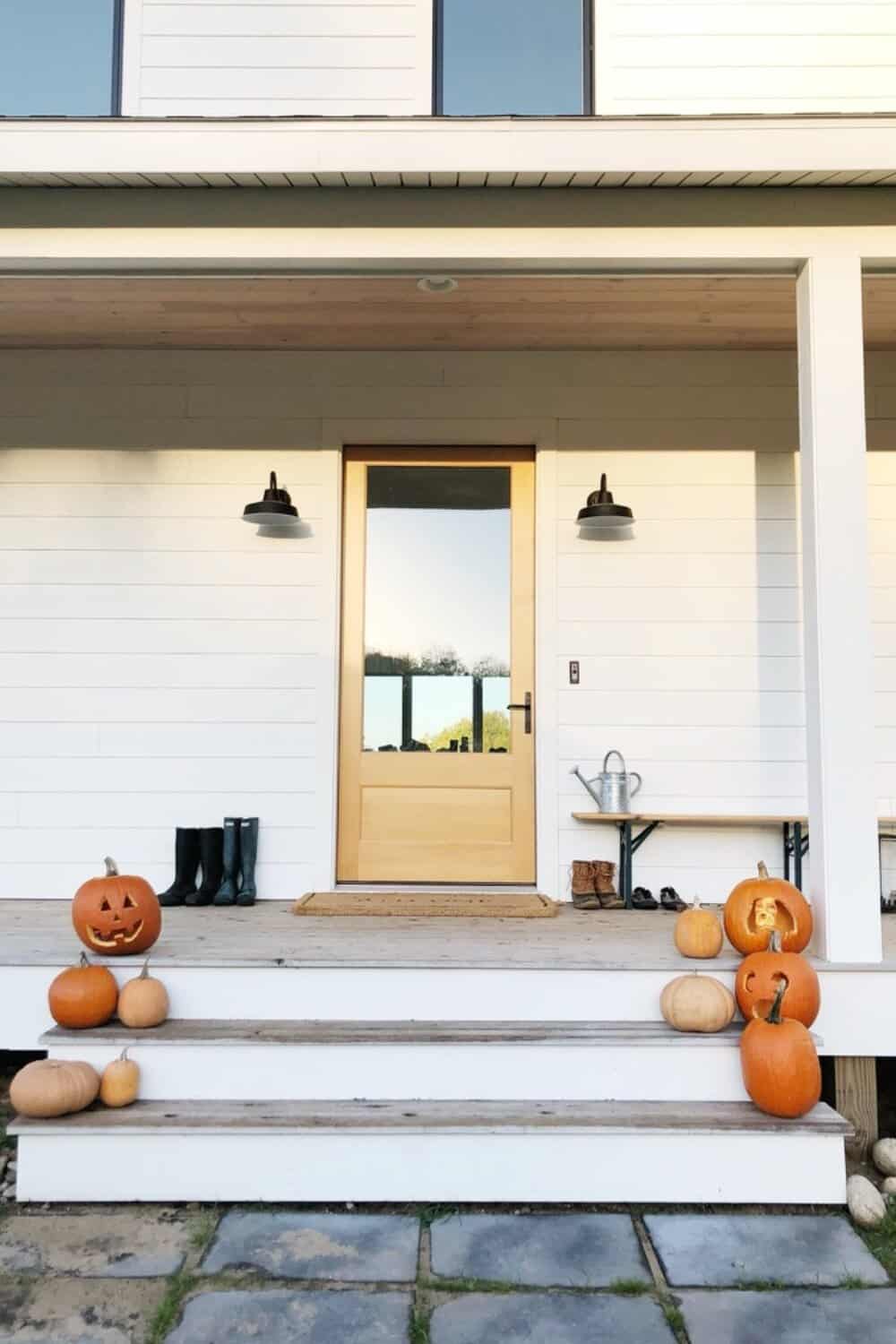 White farmhouse with wood door and pumpkins on porch 
