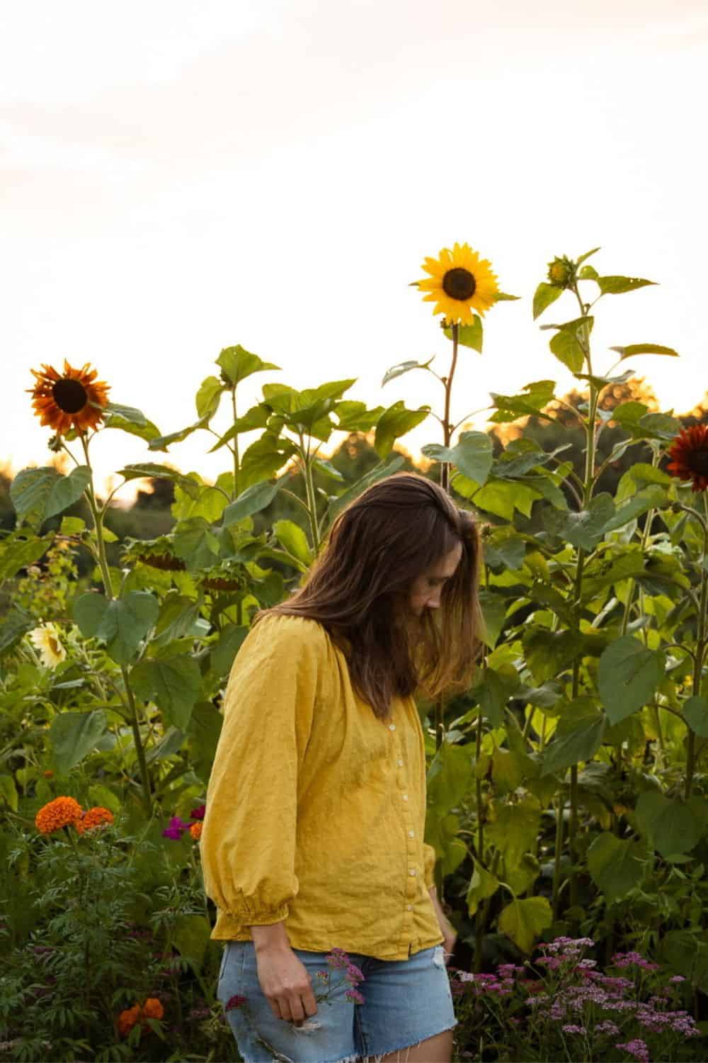 woman in yellow standing in garden with sunflowers